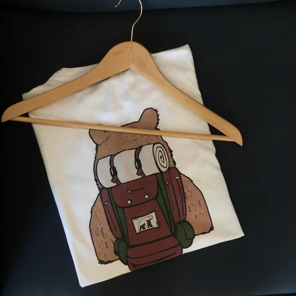 Camiseta blanca de Grizzly en una percha, con el dibujo de un oso que lleva una mochila